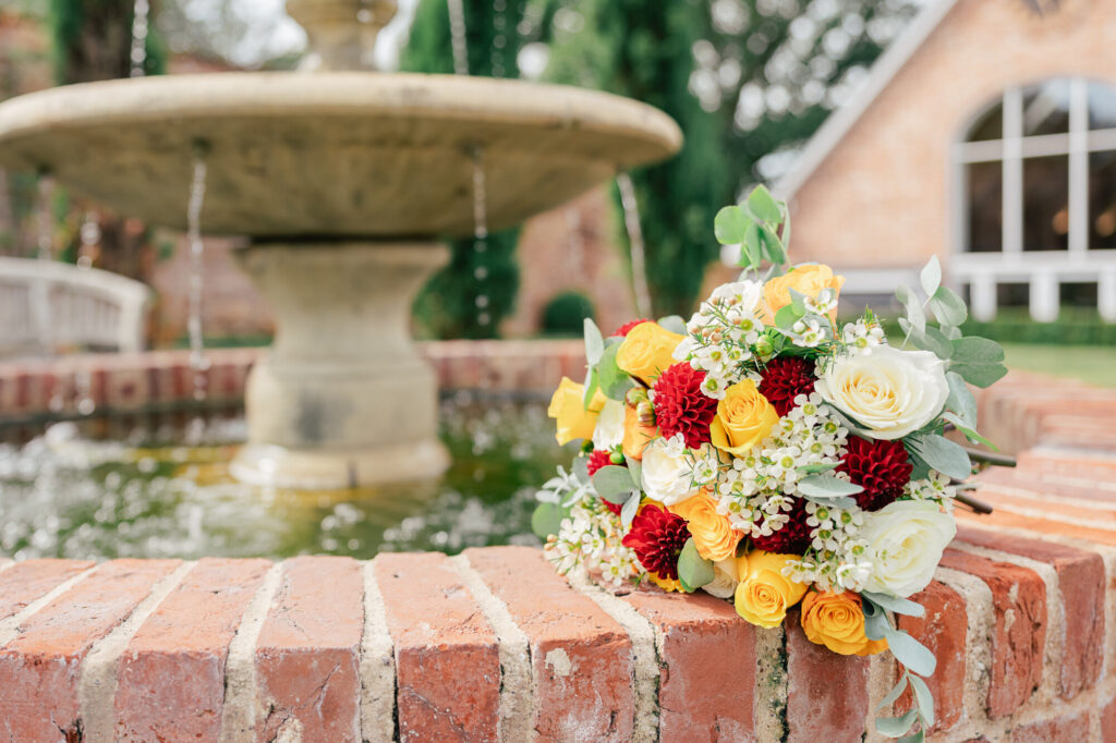 A bouquet of flowers on a brick wall next to a fountain.